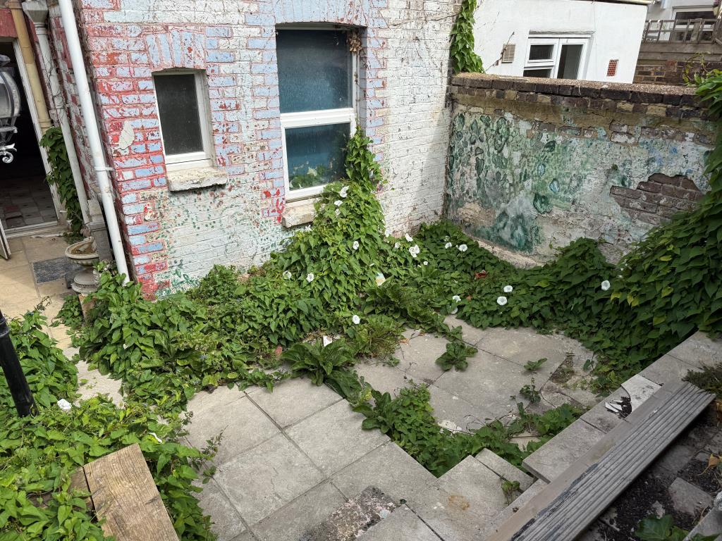 Lot: 146 - PATIO FLAT IN NEED OF REFURBISHMENT - Rear patio garden with paved area and wall
